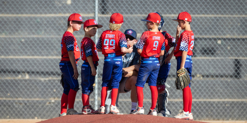 Youth sports coordinator organizing team uniforms and apparel order forms on a table with size charts and payment tracking spreadsheets.